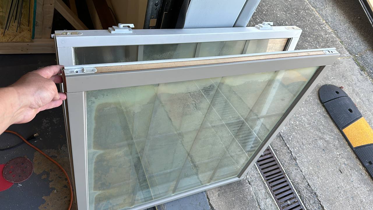 Double-pane window repair process showing foggy glass and aluminum frame components being serviced by professional technician