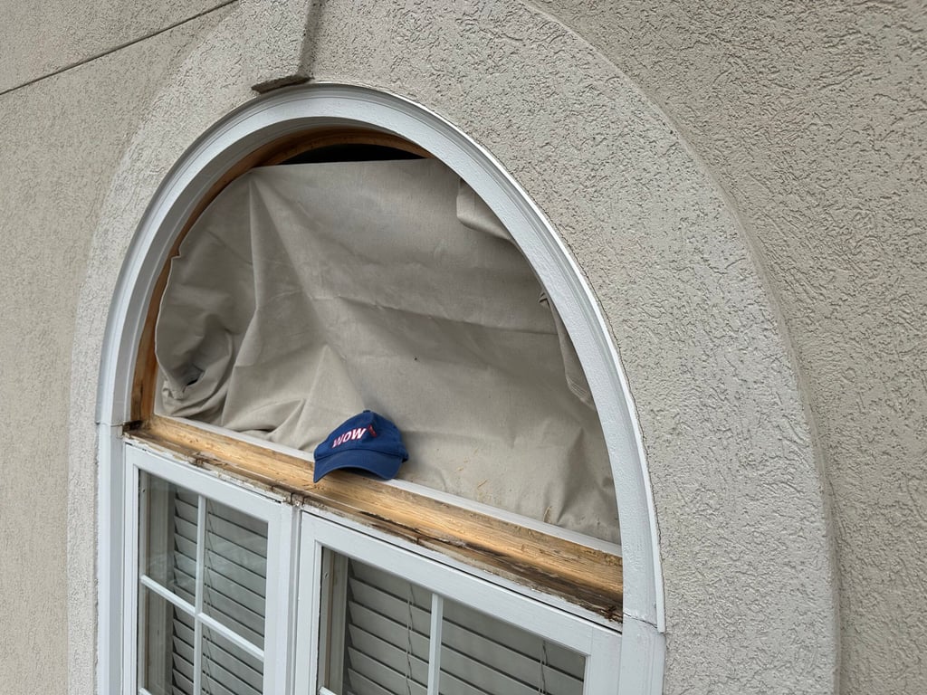 Deteriorating arched window frame with white trim and plantation shutters needing repair, showing WOW company branding