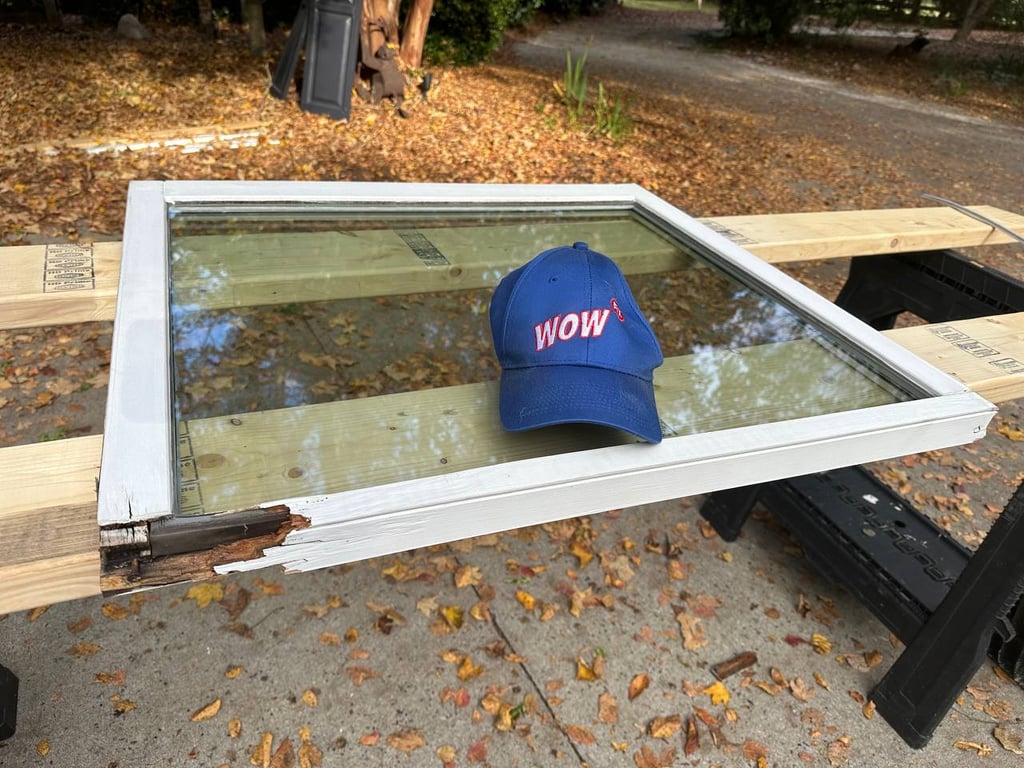 Damaged white window frame with WOW company hat showing wood rot damage, demonstrating before condition for window repair service