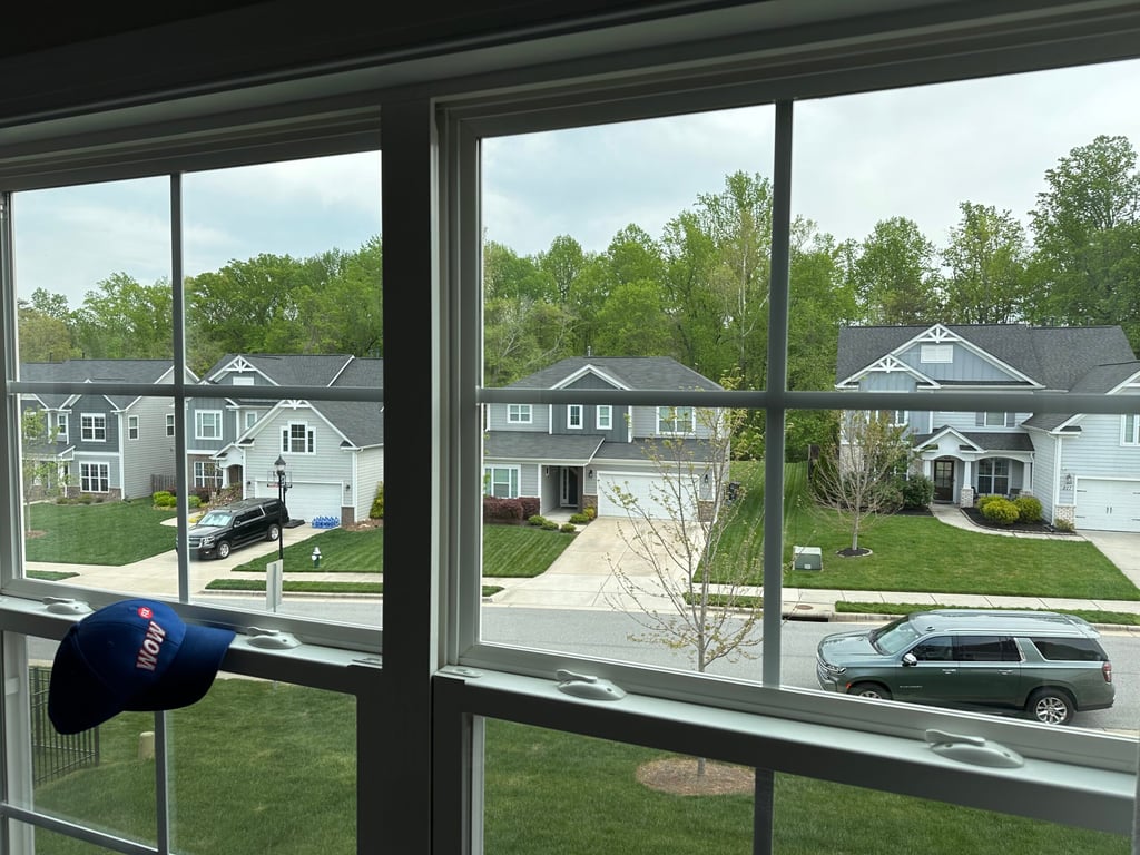 View through a clean residential window overlooking modern suburban homes in Greensboro Triad Metro area, with a WOW service cap visible