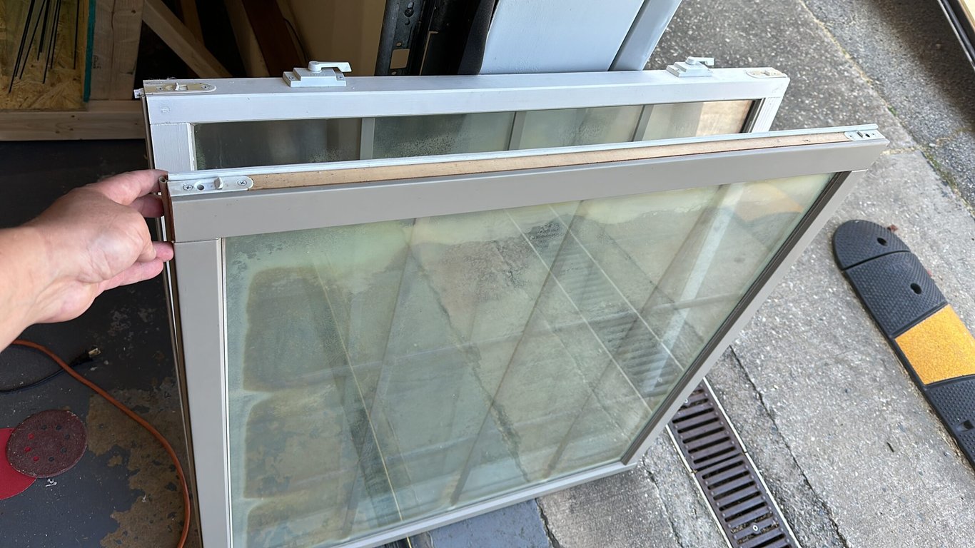 Foggy double-pane window repair in progress, showing condensation between glass panes and aluminum frame being serviced