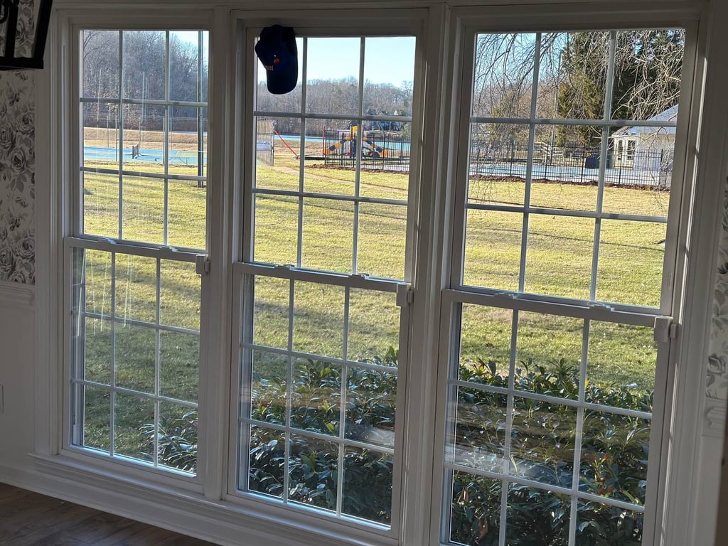Three large colonial-style double-hung windows overlooking a fenced backyard with pool and playground, showcasing professional window installation
