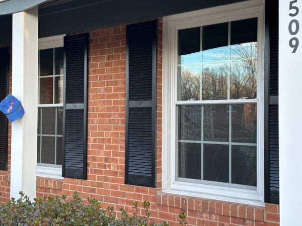 Double-hung vinyl windows with black shutters on brick home exterior in Greensboro Triad Metro area, professional window installation