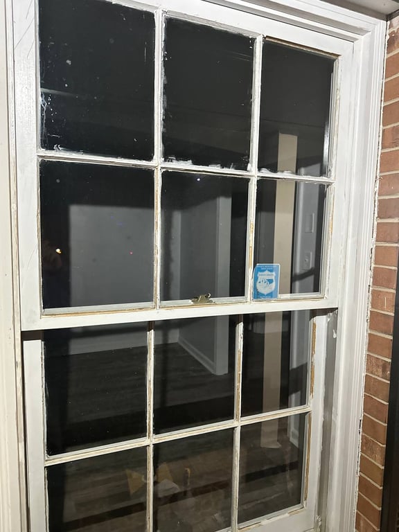 Aging 12-pane sash window with peeling paint and worn trim against brick exterior, showing signs needing professional window repair