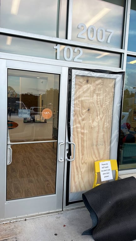 Commercial storefront with emergency board-up service showing contrast between damaged and intact glass doors with unit numbers