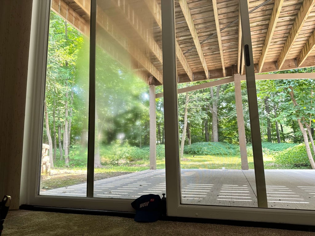 Modern sliding glass door installation overlooking forested backyard with covered porch, demonstrating professional window installation
