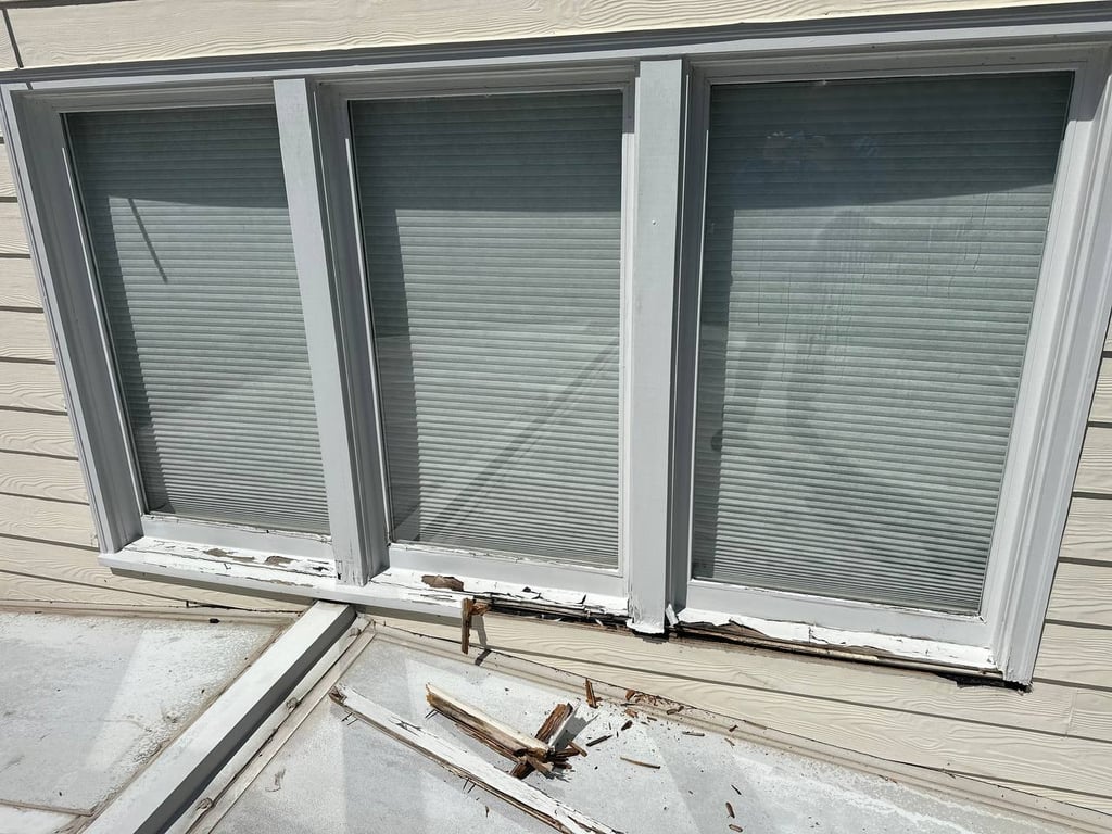 Severe window sill rot damage showing three windows with deteriorating wooden frames and splintered wood debris on concrete ledge