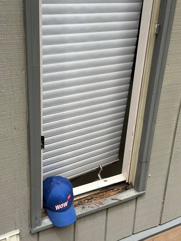 Damaged window sill with deteriorating wood frame and white horizontal blinds, showing need for professional window repair services