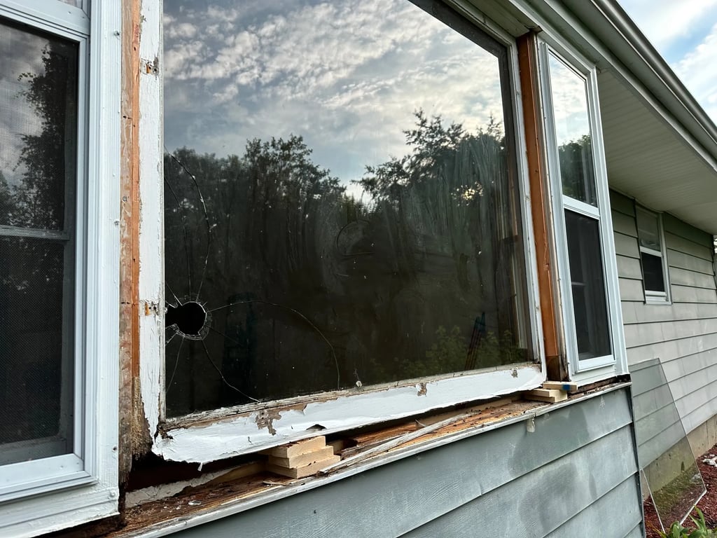 Damaged residential window with bullet hole and rotted frame showing why professional window repair services are needed in Charlotte