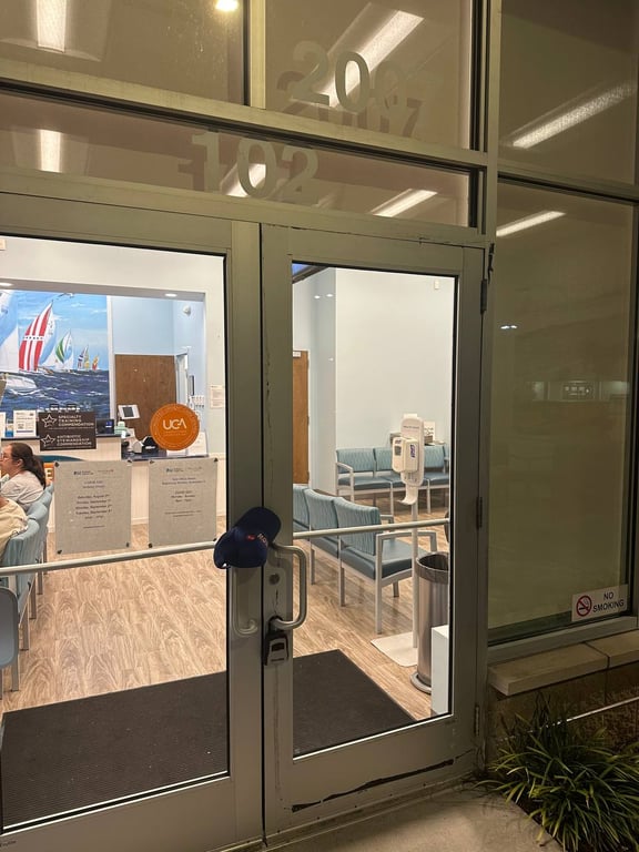 Commercial glass storefront entrance with aluminum frame doors, showing office numbers and medical waiting room interior