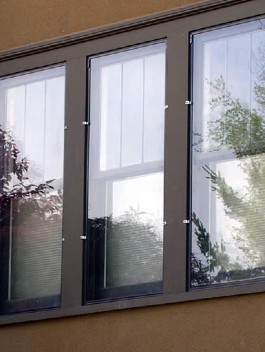 Triple panel brown-framed windows with white blinds installed on residential exterior, showing professional window craftsmanship
